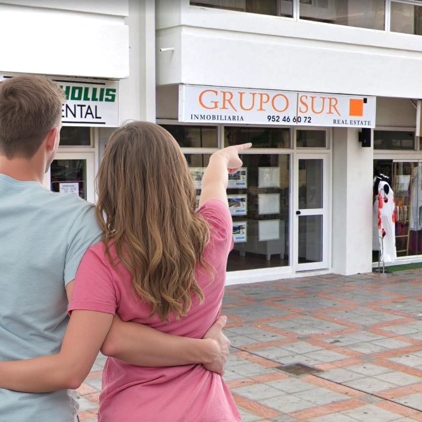 Pareja joven cogidos por la cintura y parados en medio de la calle, señalando a la fachada de Inmobiliaria Grupo Sur en Fuengirola